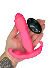 Pink silicone toy held in a hand with a remote control on a white background