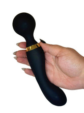 Black handheld massager with gold accent held by a hand on a white background