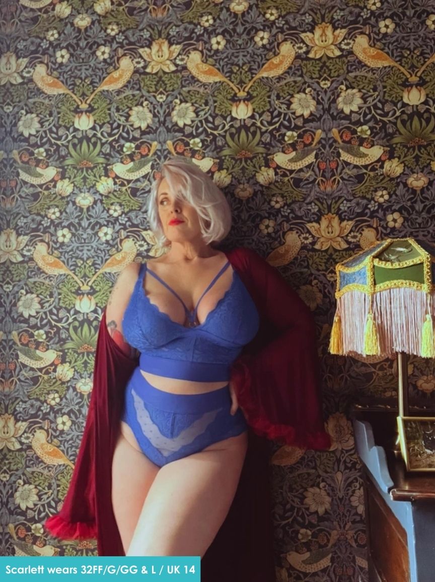 Statue of a woman in a blue lingerie set with a red cape against a patterned wall.